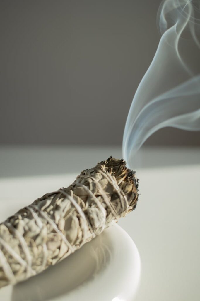 pexels-photo-20431488 A close-up of a burning sage stick emitting smoke on a white plate.