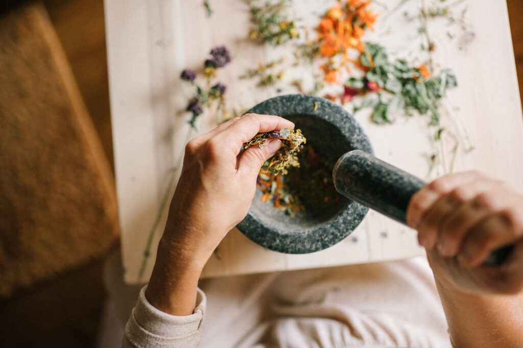 pexels-photo-5480054 Top view of hands grinding dried herbs using a mortar and pestle on a wooden table.